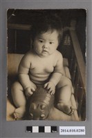 藏品(嬰兒車中把玩存錢筒玩具的孩童)的圖片