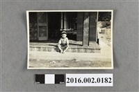 藏品(一位坐在房舍外廊地板的小男孩)的圖片