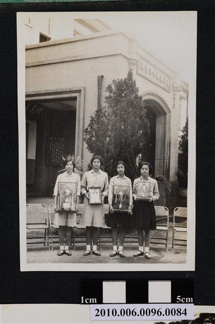 四位女孩手捧獎盃及獎牌站立於省立屏東女子中學建築物前合影之照片 (共2張)