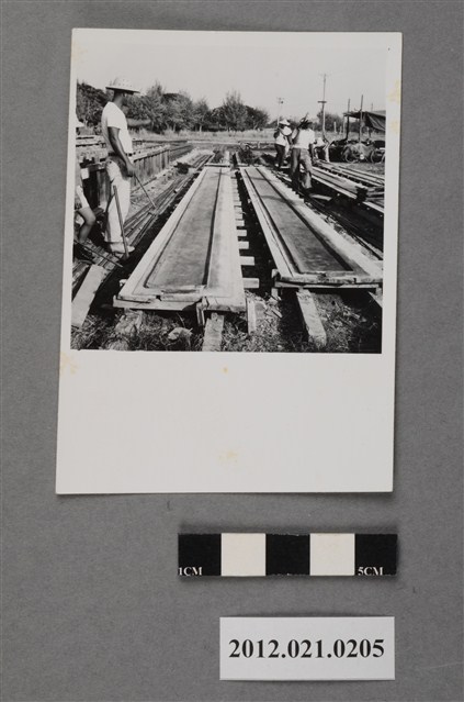 基地內工程斗笠工人兩人合力扛物品 (共2張)